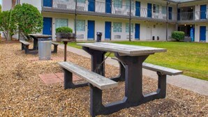 A building with a row of rooms, each with a blue door and a balcony. There are picnic tables in the foreground. - 1 Queen Bed | Smoking (Pascagoula)