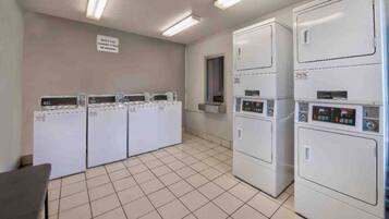 A laundry room with multiple washing machines and dryers, a tiled floor, and a sign on the wall.