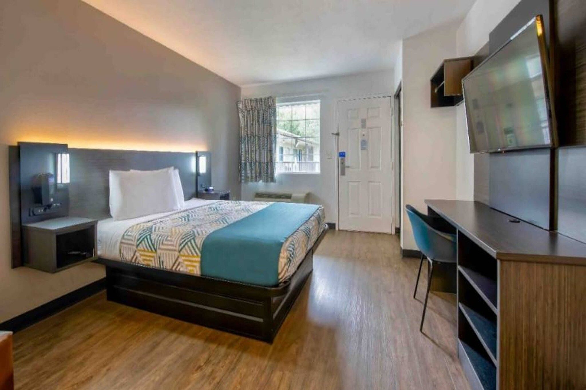 Une chambre d’hôtel avec un lit, un bureau, une télévision et une fenêtre avec des rideaux.