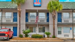 A 6 extended stay office building with a sign, two palm trees, an American flag, and a red truck parked in front. - 1 Queen Bed | Smoking (Pascagoula)