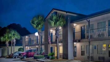 A multi-story hotel with a parking lot, palm trees, and a red car parked outside.