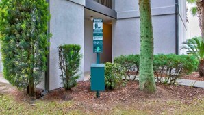 A building entrance with a waste station sign, surrounded by trimmed shrubs and a palm tree. - 1 Queen Bed | Smoking (Pascagoula)
