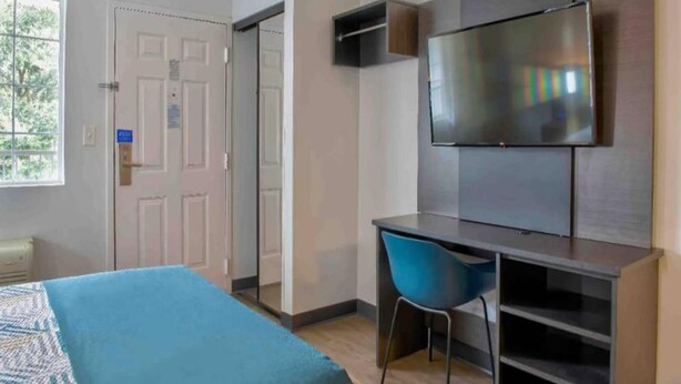 A hotel room with a bed, a desk, a chair, a television, and a door. - 1 Queen Bed | Smoking (Pascagoula)