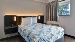 Habitació d'hotel amb un llit, taules de nit, una finestra amb cortines i una làmpada de paret.