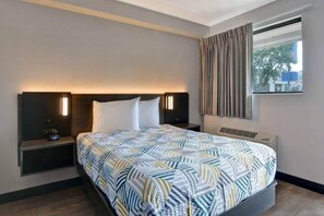 A hotel room with a bed, bedside tables, a nightstand, a window with curtains, and a wall-mounted light fixture. - 1 Queen Bed | Non-Smoking, Kitchen (Jacksonville)