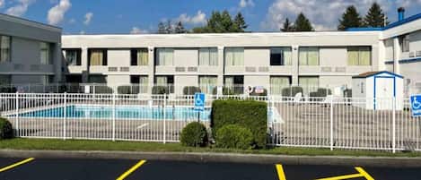 A hotel with a swimming pool, parking spaces, and a fenced area.