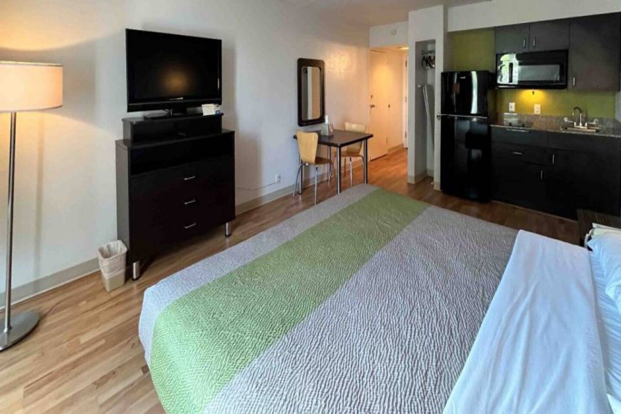 Habitación de hotel con cama, escritorio, televisión, espejo y kitchenette.