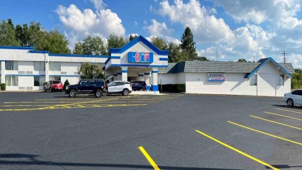 Un estacionamiento con espacios delimitados, un edificio de fachada azul y blanca, y un letrero que dice '6 Star'.