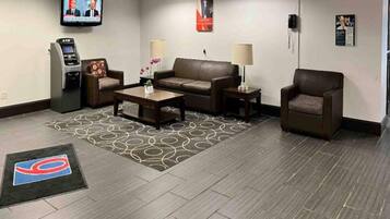 Een hotel lobby met een bank, fauteuils, een salontafel, een televisie en een minibars.