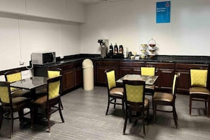 A hotel dining area with a long counter, multiple chairs, and a coffee station. - Studio 6 Suites Clarion, Pa_1 Queen Bed (Clarion)
