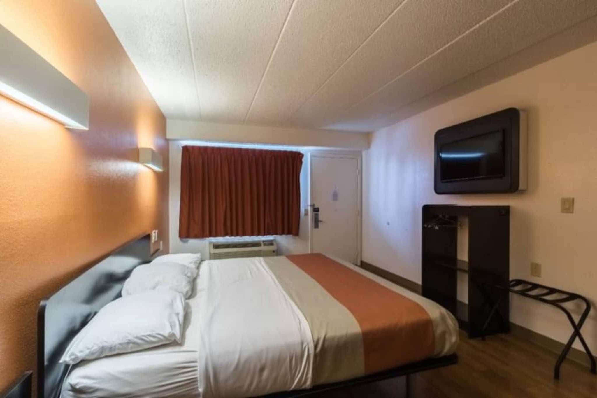 Ett hotellrum med en säng, en tv som är monterad på väggen och ett fönster med gardiner.