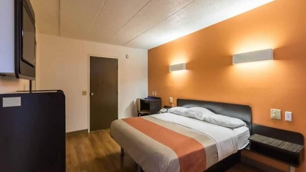 A hotel room with a bed, a desk, a chair, a TV, and a door. - 1 King Bed | Non-Smoking (CRAWFORDSVILLE)