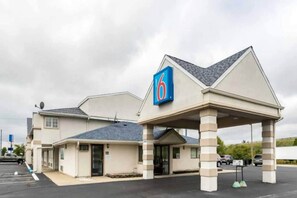 A motel with a '6' sign, a covered parking area, and a single-story building. - 1 King Bed | Non-Smoking (CRAWFORDSVILLE)