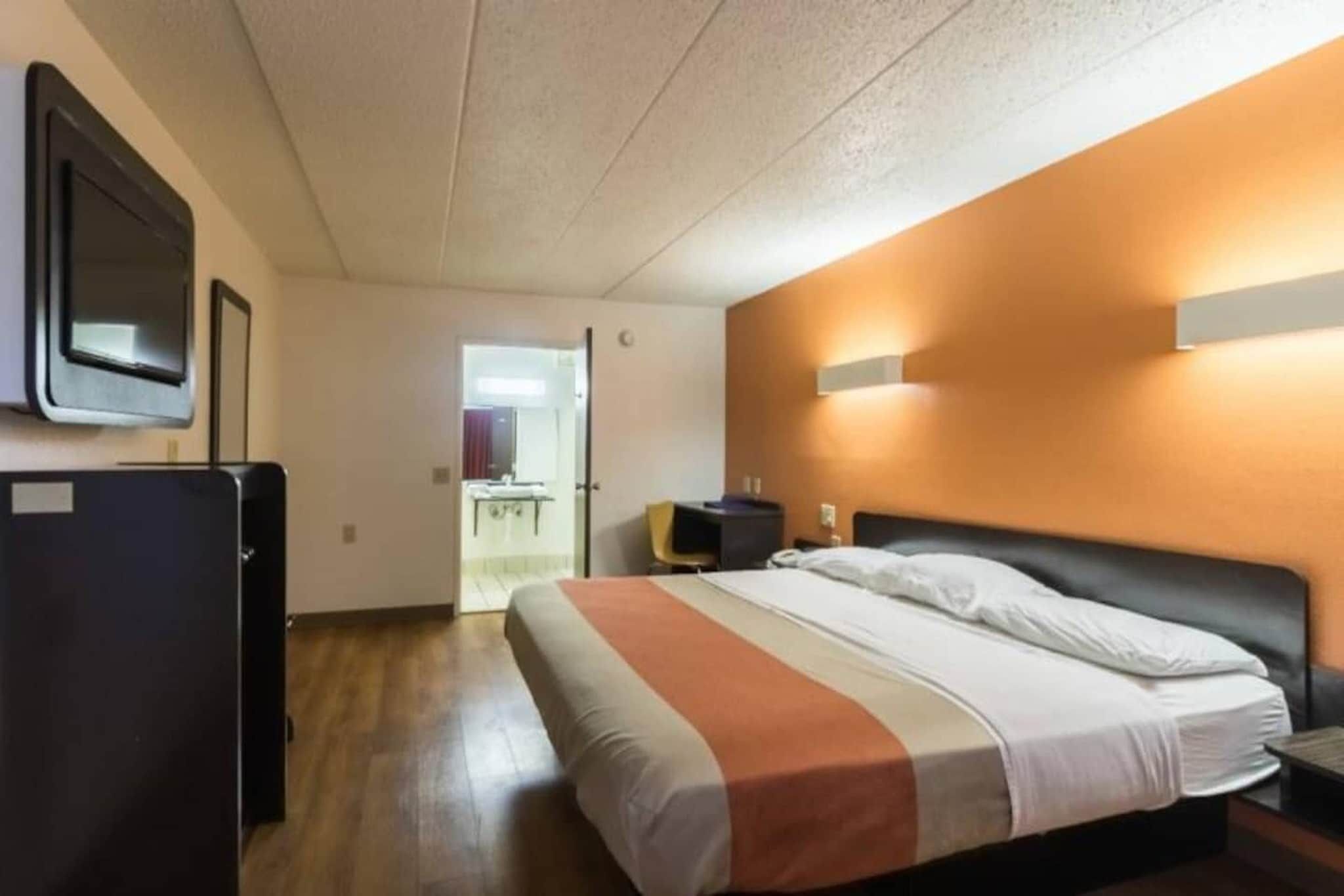 A hotel room with a bed, a desk, a chair, a mirror, and a television.