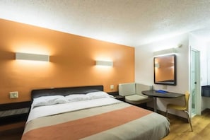 A hotel room with a bed, a desk, a chair, and a mirror.