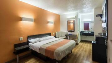A hotel room with a bed, bedside table, chair, and a small desk with a mirror.
