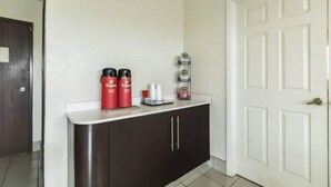 A hallway with a white door, a dark brown cabinet, and a small shelf with red containers and a white tray. - 1 King Bed | Non-Smoking (CRAWFORDSVILLE)