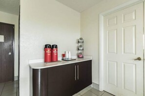 A hallway with a white door, a dark brown cabinet, and a small shelf with red containers and a white tray. - 1 King Bed | Non-Smoking (CRAWFORDSVILLE)