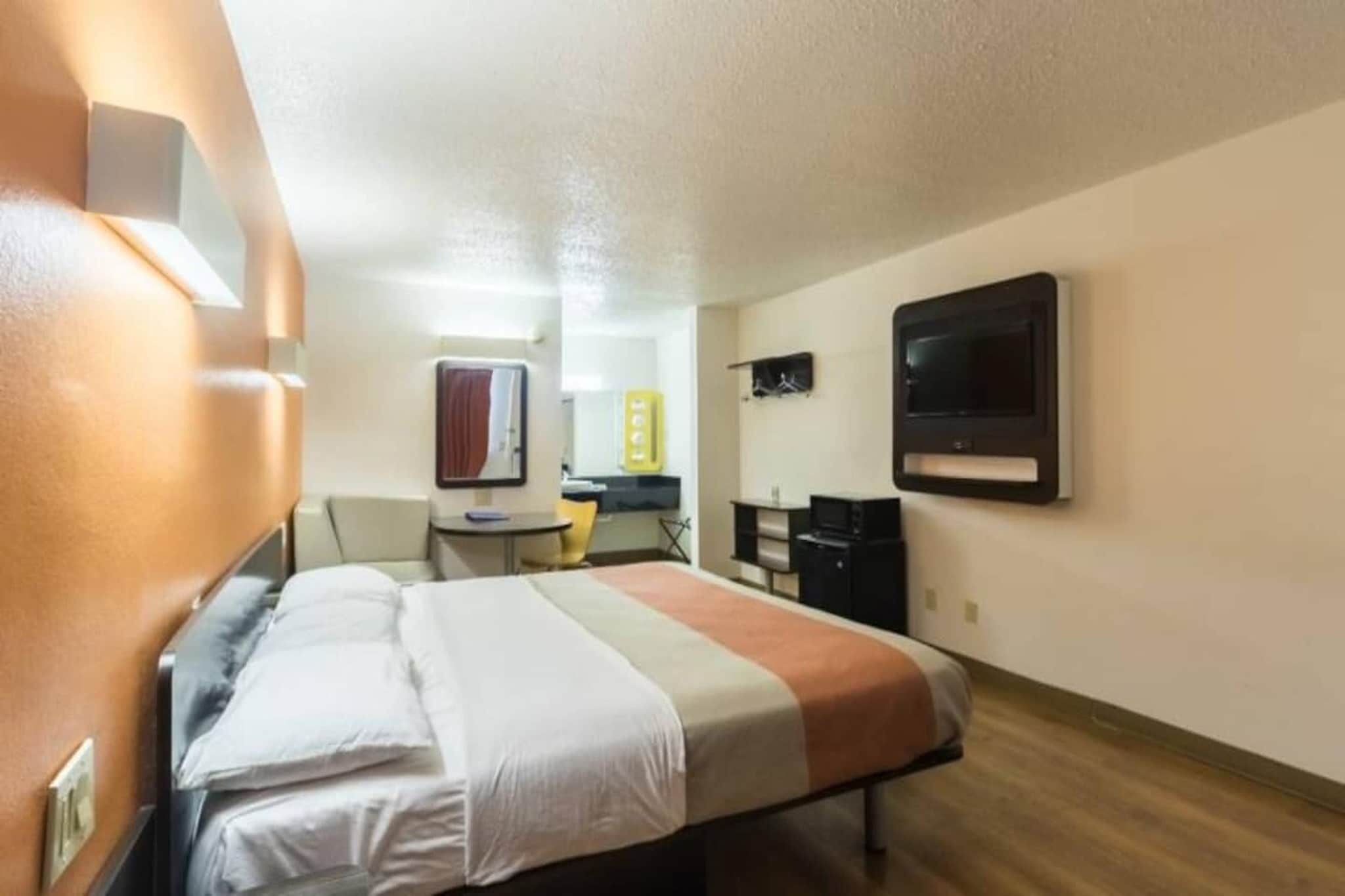 A hotel room with a bed, a desk, a chair, a TV, and a mirror.