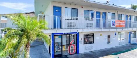 Ein Motel mit blauer Fassade, einem Balkon mit Geländern und einer Palme im Vordergrund.