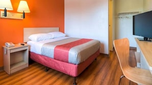 Ett hotellrum med en säng, ett sängbord, en lampa, en stol och en tv.