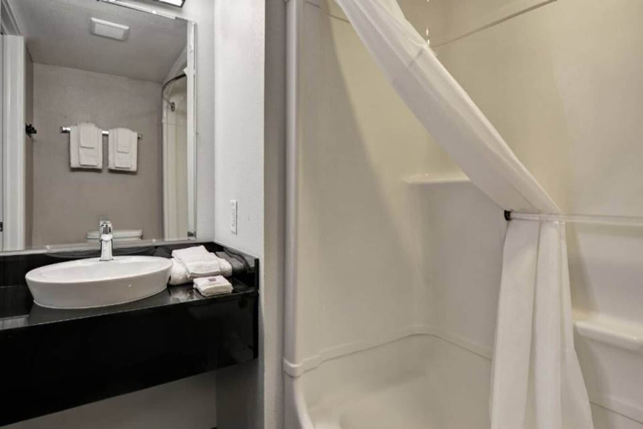 Une salle de bain avec un lavabo blanc, un miroir et un rideau de douche.