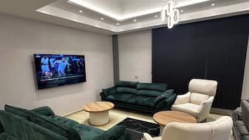 A modern living room with a flat-screen TV, green and white sofas, a coffee table, and a black accent rug.