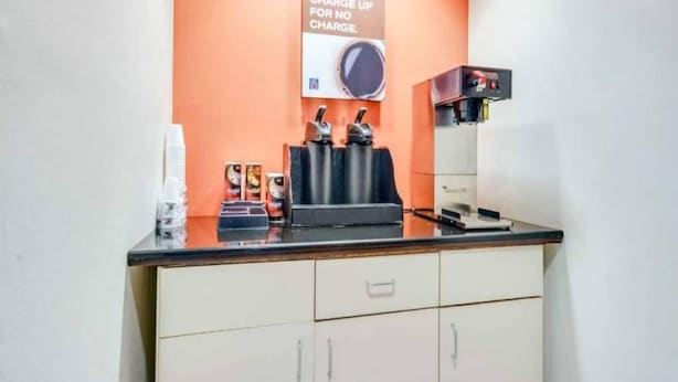 Una estación de café con una máquina de café, tazas y un cartel que ofrece café gratis por la mañana.