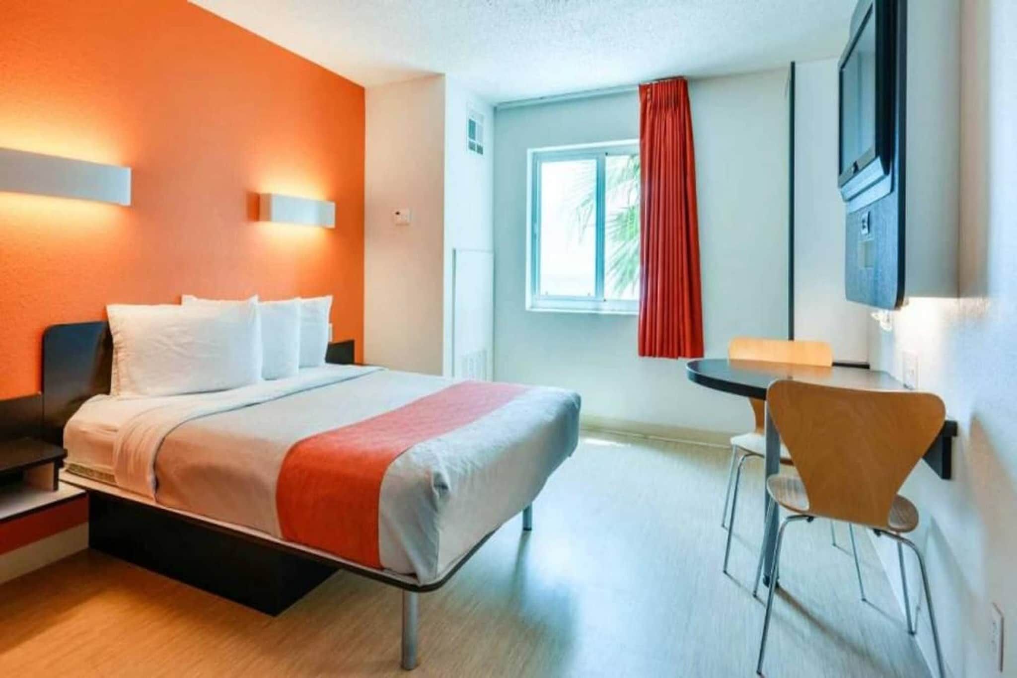 A hotel room with a bed, bedside table, chair, and a TV mounted on the wall.