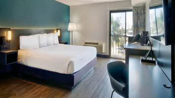 Une chambre d’hôtel comprenant un lit, une table de chevet, une lampe, un bureau, une chaise et une grande fenêtre.