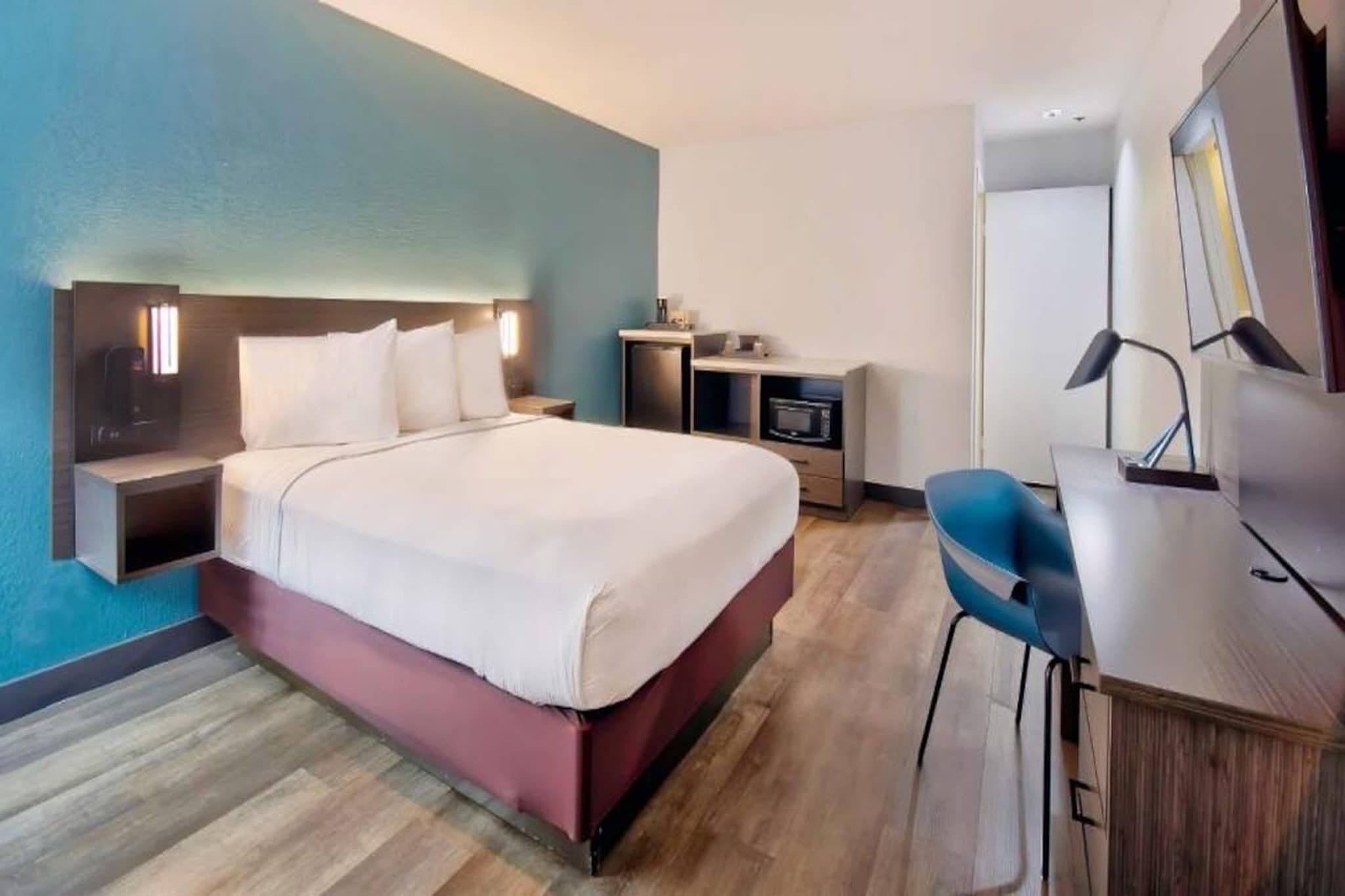 A hotel room with a bed, bedside table, lamp, desk, chair, and a mirror.