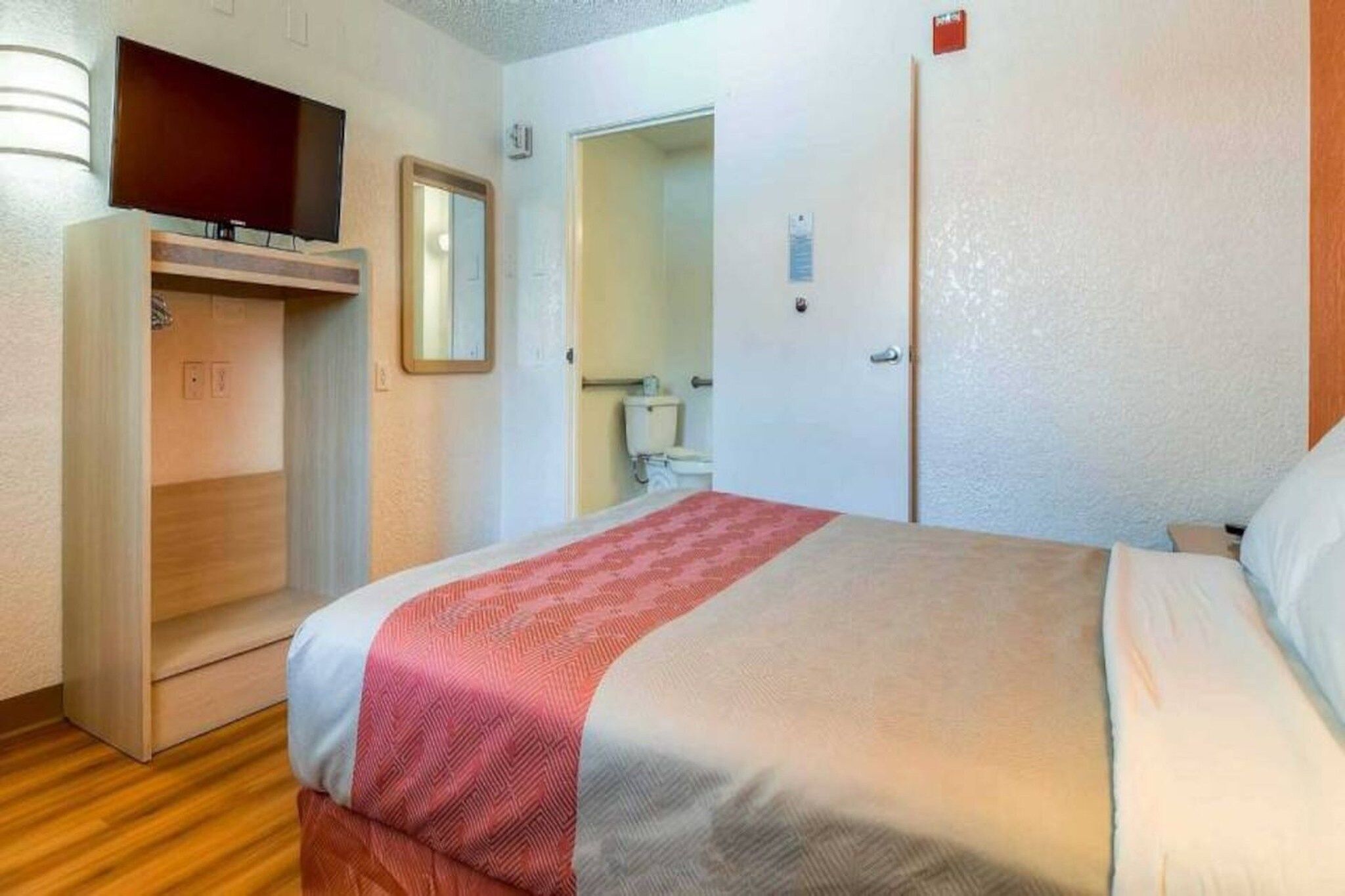 A hotel room with a bed, a wardrobe, a mirror, and a bathroom visible through an open door.