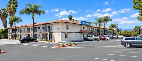 A motel with a 'Welcome' sign, multiple parking spaces, and palm trees.