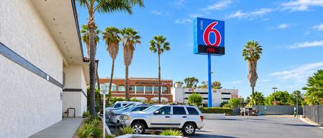 En parkeringsplads med et skilt, der viser '6 Motel', palmer og en bygning med et skilt for 'The Grand Canyon Hotel'.