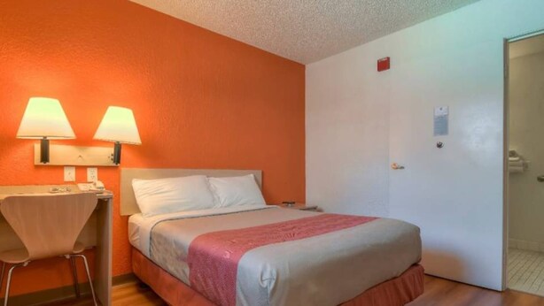 Quarto de hotel com cama, escrivaninha e cadeira, e uma porta.