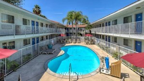 Um hotel com piscina central rodeada por espreguiçadeiras e guarda-sóis, com vários andares e varandas.