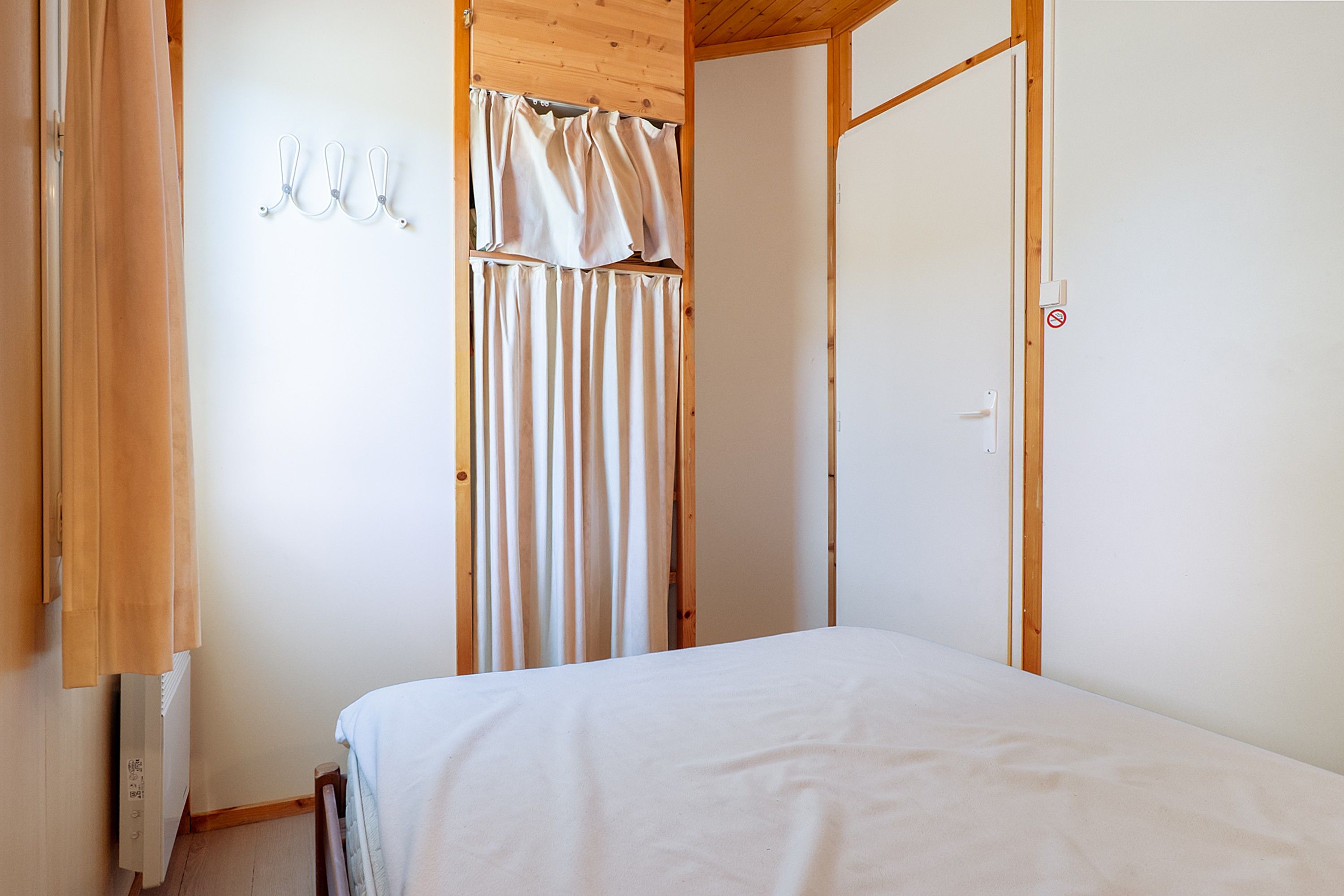 Un dormitorio con cama, techo de madera, puerta blanca y cortina.