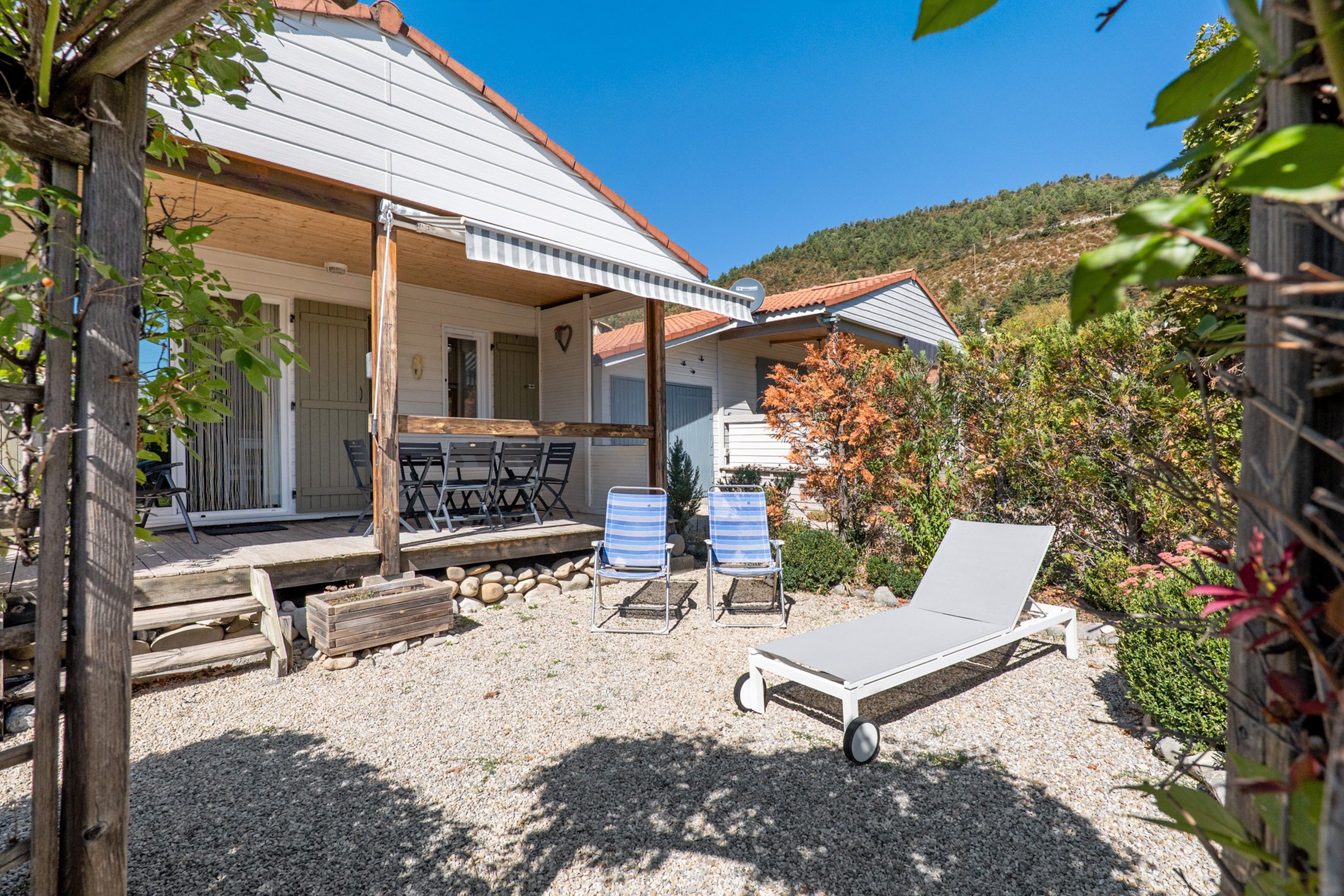 A covered outdoor seating area with a table and chairs, a lounge chair, and a barbecue grill.
