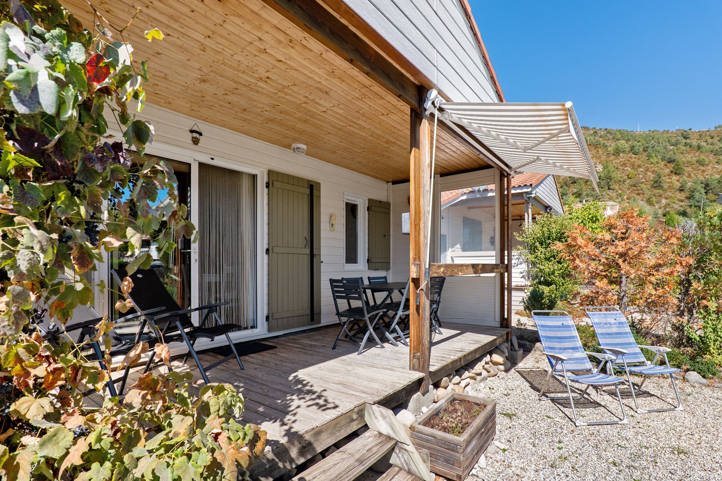 Una terraza de madera con mobiliario exterior, un área de estar cubierta y vistas a una colina.