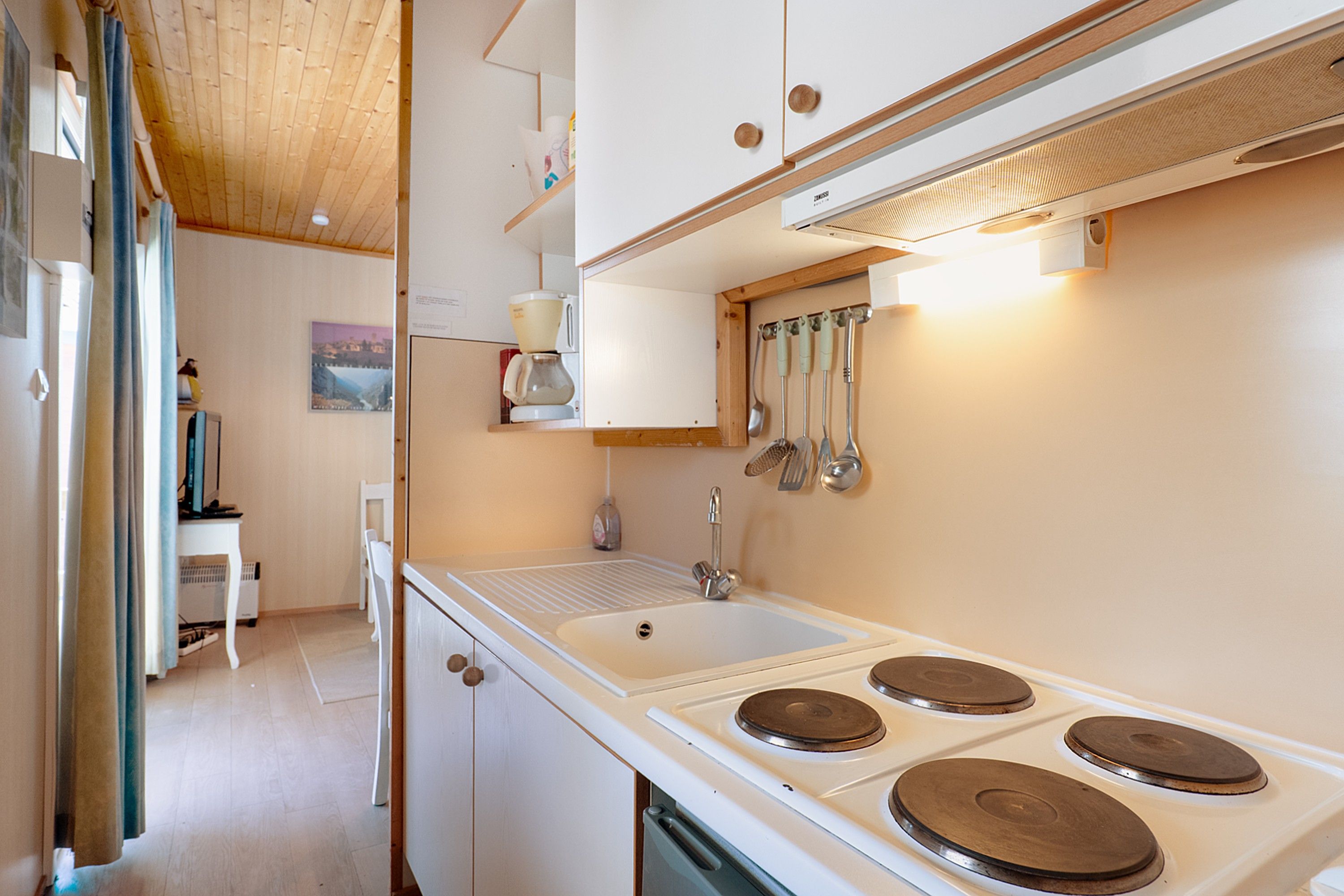 A compact kitchen with a sink, stove, and hanging utensils.