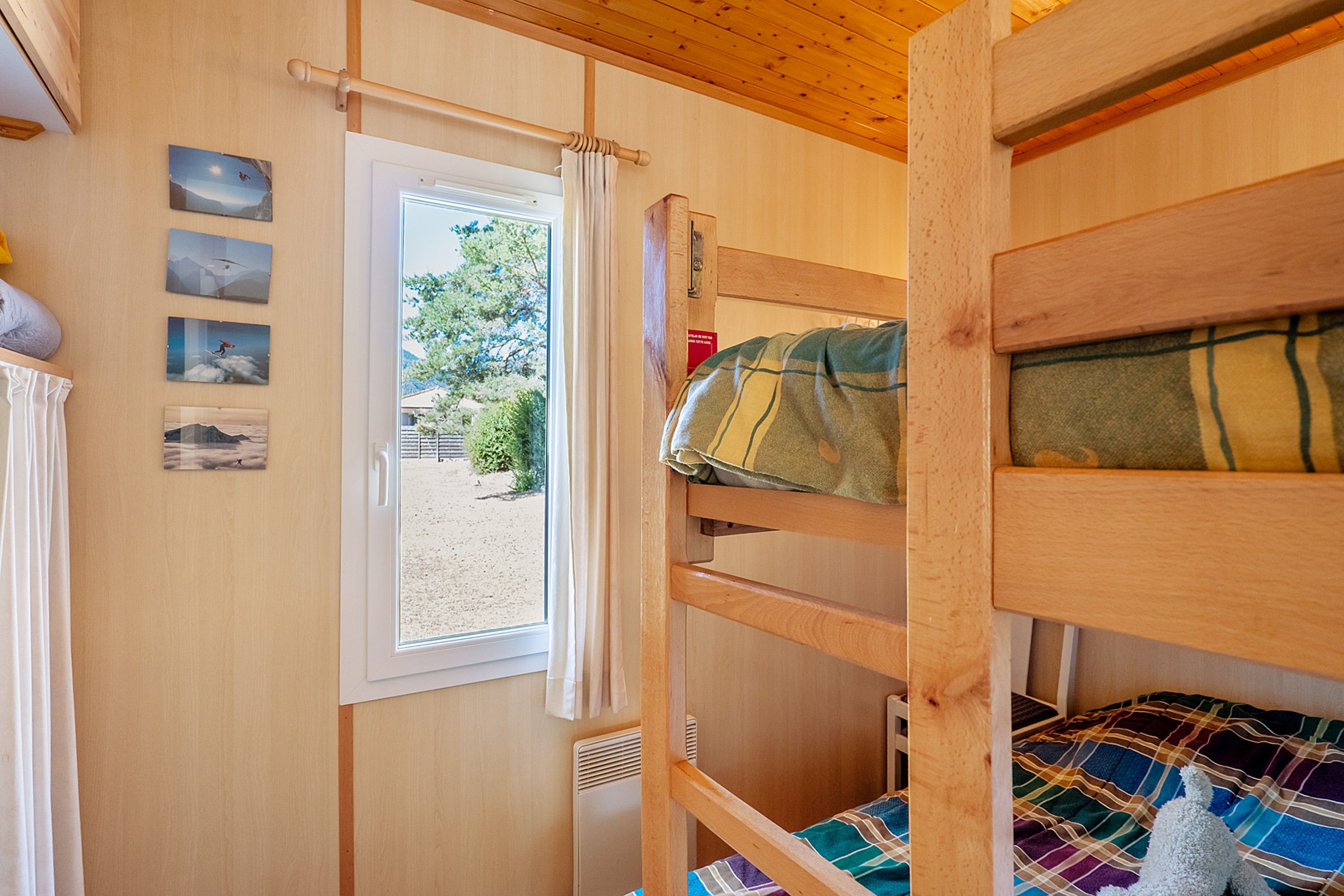 Une chambre avec un lit superposé, une fenêtre, des murs en bois et une vue sur un jardin.