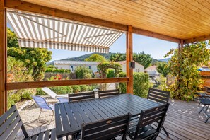 An outdoor patio with a table and chairs, surrounded by greenery and a view of houses in the distance. - Chalet 'Castellane' with Mountain View, Shared Pool and Wi-Fi (Castellane)