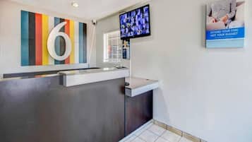 A reception desk with a modern design, a large number '6' on the wall, a television screen, and a poster advertising budget extension.