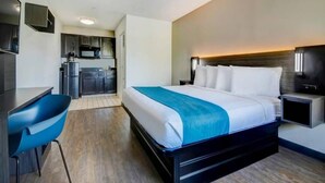 Quarto de hotel com cama, escrivaninha, cadeira, cozinha compacta e televisão.