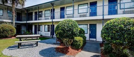 A two-story motel with a covered parking area, a picnic table, and well-maintained landscaping.