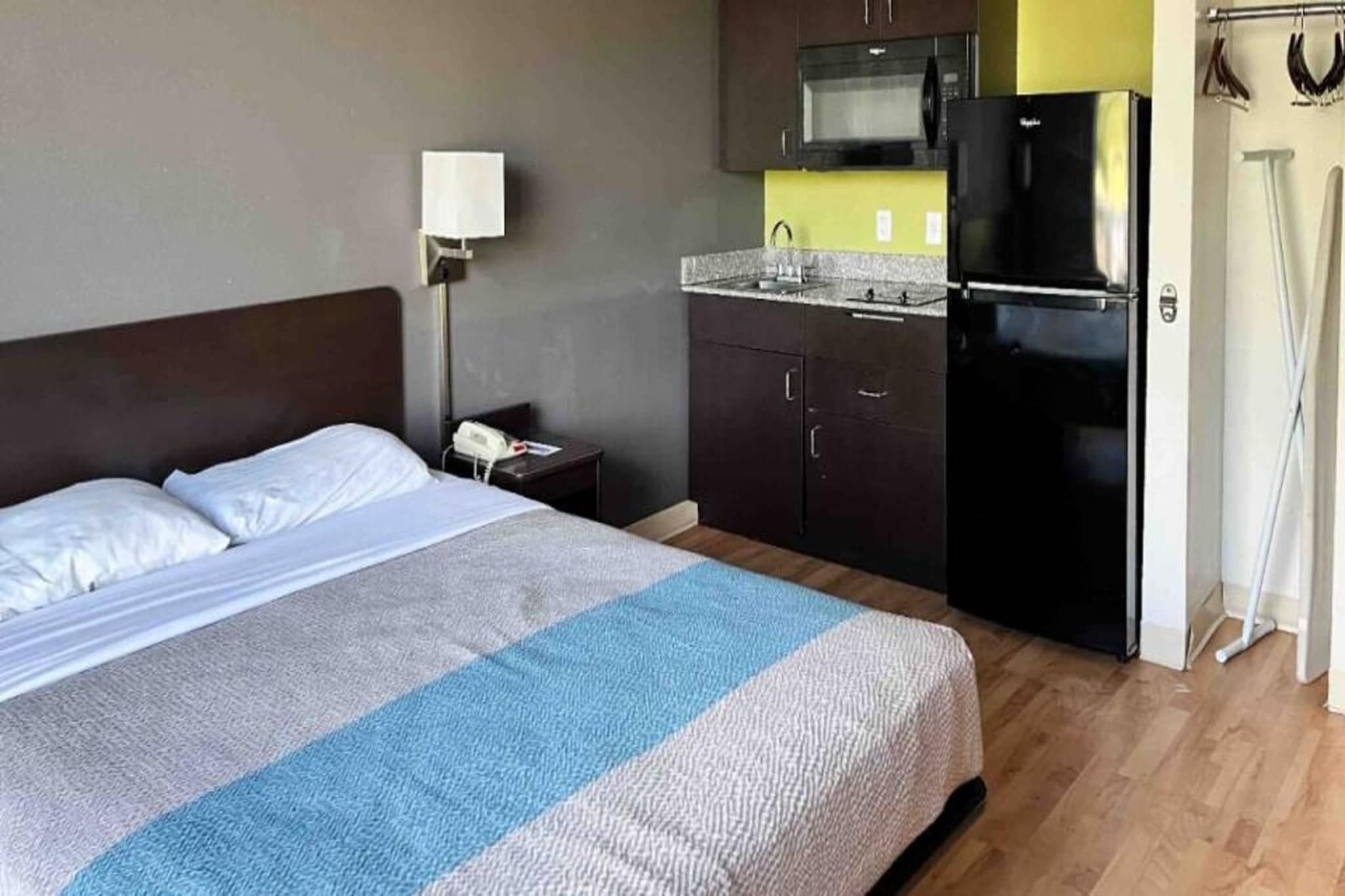 A hotel room with a bed, a nightstand, a microwave, and a refrigerator.