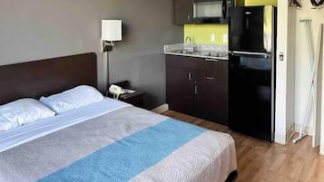 A hotel room with a bed, a nightstand, a microwave, and a refrigerator.