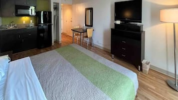 Habitació d'hotel amb llit, escriptori, televisió i petita cuina.