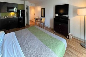 A hotel room with a bed, a desk, a television, and a kitchenette. - 1 Queen Bed | Smoking, Kitchen (Clarion)