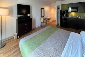 A hotel room with a bed, a desk, a television, a mirror, and a kitchenette.